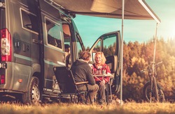 Caucasian Couple Playing Chess Next to Their Camper Van RV During Vacation Camping Time. Recreational Vehicles and Road Trip Theme.