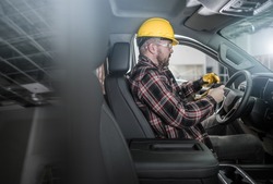 Caucasian Construction Worker Wearing Hard Hat and Gloves Inside Commercial Pickup Truck Inside a Warehouse Industrial Building.