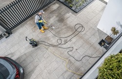 Caucasian Home Owner Pressure Washing His Dirty Driveway Aerial Photo. Keeping Concrete Driveway Bricks Clean. 