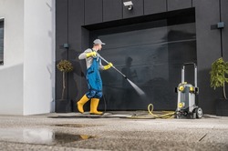 Caucasian Men Pressure Washing His Garage Gate Using Powerful Washer. Keeping the Gate and Driveway Clean. 