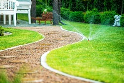 Backyard Residential Garden Grass Field Sprinklers in Action. Garden Path.