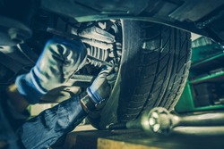 Car Mechanic Fixing Tie Rod and Steering System While Being Under the Vehicle. Car Maintenance in the Professional Service.