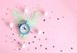 Party Time Layout with Little Clock, Green Palm Leaves and Silver Confetti of Star Shape on a Pastel Pink Background. No Text. Top-Down View. Flat Lay Composition ideal for Banner, Newsletter, Card.