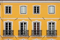 Traditional house with yellow facade and tall windows with balconets in Lisbon, Portugal.