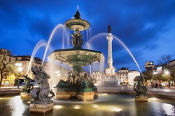 Fountain on Rossio Square at night in Lisbon, Portugal. Baroque style artwork with mythical creatures sculptures. Column of Dom Pedro IV in the background.