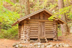 Old solid log cabin shelter hidden among green trees in the forest