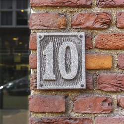Weathered aluminum house number ten on a red brick wall