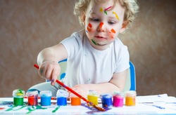 Cute little child painting with paintbrush and colorful paints