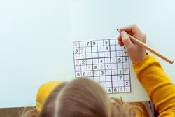 Adorable teen girl solving sudoku at desk at school or at home. View from above