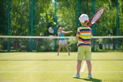 Little cute boy playing tennis on green court