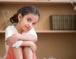Portrait of cute little hispanic girl sitting on carpet at home