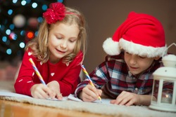 Two happy children writing letter at Christnas eve to Santa Claus at home near New Year tree