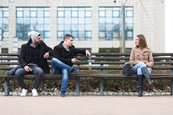 Three smiling students on a bench in a park together talking and smiling