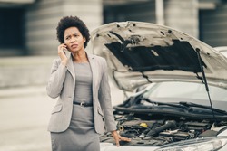 Worried black business woman calling for help after her car breakdown on the street.