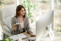 An attractive  business woman drinking coffee while using a computer in her home office.