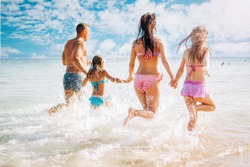 Happy family having fun on the beach. They with holding hands running and splashing in the sea.