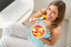 Beautiful young smiling woman eating fruit salad in the morning. Looking at camera.