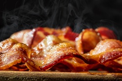 Closeup photo of a pile of freshly cooked hot crispy bacon resting on a wood cutting board