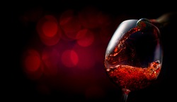 Wine pouring into wineglass on dark red background