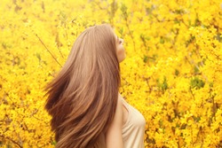 Beautiful young woman with long healthy hair against yellow flowers background. Girl with blowing hairstyle portrait