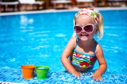 Cute baby girl in sunglasses playing with toys in the swimming pool outdoors