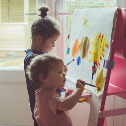 Two little girls painting on the easel, selective focus, toned