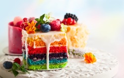 Various slices of cakes on a white tray: rainbow cake, raspberry cake and almond cake. Sweets decorated with fresh berries and flowers for holiday