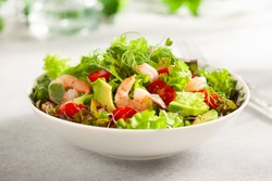 Fresh summer salad with shrimp, avocado and tomato cherry in bowl on light table. Concept of healthy eating.