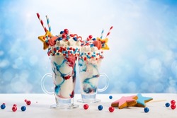 Crazy milk shake with ice cream,whipped cream, marshmallow,cookies and colored candy in glass. Sweet dessert for Fourth of July. Idea milkshake for Patriotic day.