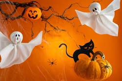 Halloween ghosts, pumpkins and black cat on orange background. Happy Halloween holiday concept. Handmade decoration for festival party.