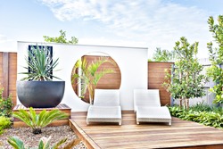 Outdoor relaxing area with the wooden decoration and trees from the garden including big and black vase, the pot includes a green leaf plant which also covered the area with walls at daytime