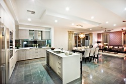 Modern and shiny kitchen with dining and living area, including a counter top and kitchenware on the reflective tiles, there are lights flashing at night
