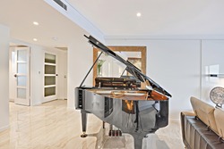 Shiny piano with black color in the luxurious living room of a house or hotel, the floor is made in tiles through the hallway, there are white walls cover the area