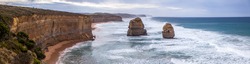 A huge panorama of orange steep cliffs and rocky islands in the ocean near Twelve Apostles Sea Rocks near Great Ocean Road, Port Campbell National Park, Australia. Wide waves rolling to the seashore. 