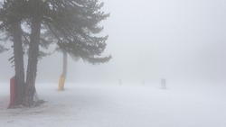 Silhouette of a cross country skier barely visible in very dense fog. Bad weather on ski resort, soft focus