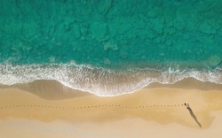 Woman walks on the beach along breaking waves leaving footprints on a sand. Aerial view directly above