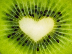 Green fruit kiwi close up with heart, green background. Kiwi fruit in the form of heart. Kiwi with seeds close-up. Heart using kiwi fruit for Valentine's day. Beautiful kiwi whole screen with heart.