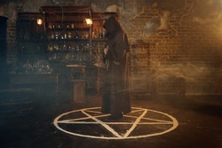 Male exorcist in hood standing in the magic circle