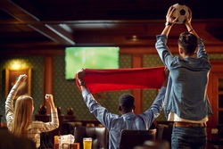 Happy football fans with red scarf and ball in bar