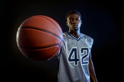 Basketball player shows a ball, black background