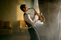Young elegant man playing gold alto saxophone in misty room