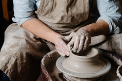 pottery, workshop, ceramics art concept - closeup on male hands sculpt new utensil with a tools and water, man's fingers work with potter wheel and raw fireclay, front close view
