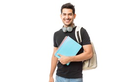 Portrait of smiling young college student with books and backpack against white background
