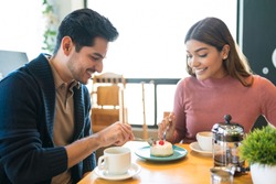 Smiling young couple sharing dessert at table in cafe