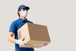 Young delivery man wearing face mask and gloves while carrying cardboard box during coronavirus outbreak