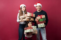 Cheerful Latin family carrying a lot of Christmas presents and getting ready to deliver them on a studio