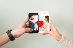 Close up of couple joining two smartphones together with a photo of an attractive man and young woman in love holding a red heart. Love concept