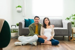 Attractive couple in love expecting their new baby. Handsome man and beatiful pregnant woman hugging while sitting on the floor at home