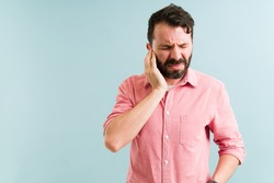 Worried man in his 30s aching and listening to a ringing in his ear. Pained man with touching his ears because of an infection 