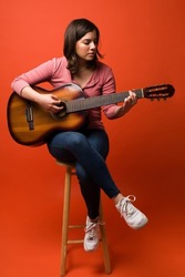 Full length of a beautiful young woman sitting on stool and playing the acoustic guitar 